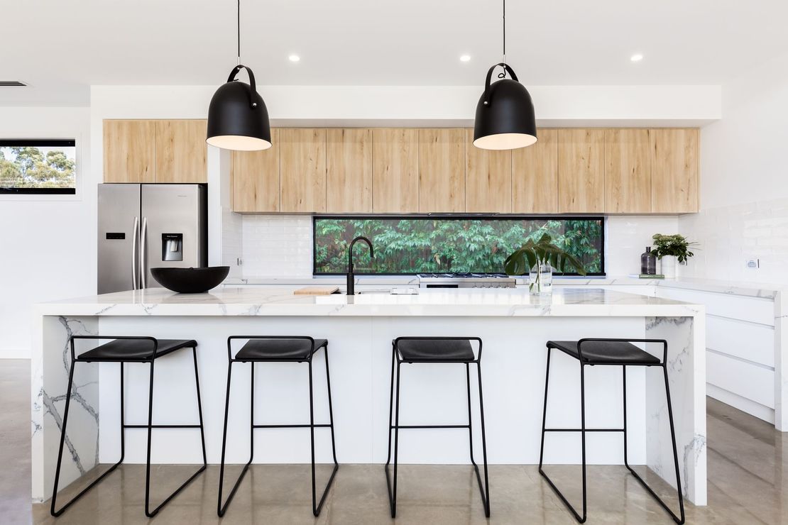 A kitchen with a large island , stools , and a refrigerator.