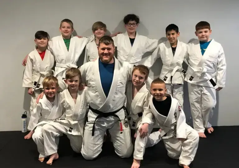 Group of children and a man in martial arts uniforms, posing in a gym.
