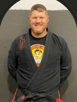 Man in black martial arts uniform smiling. Red belt, black gi. Black, grey background.