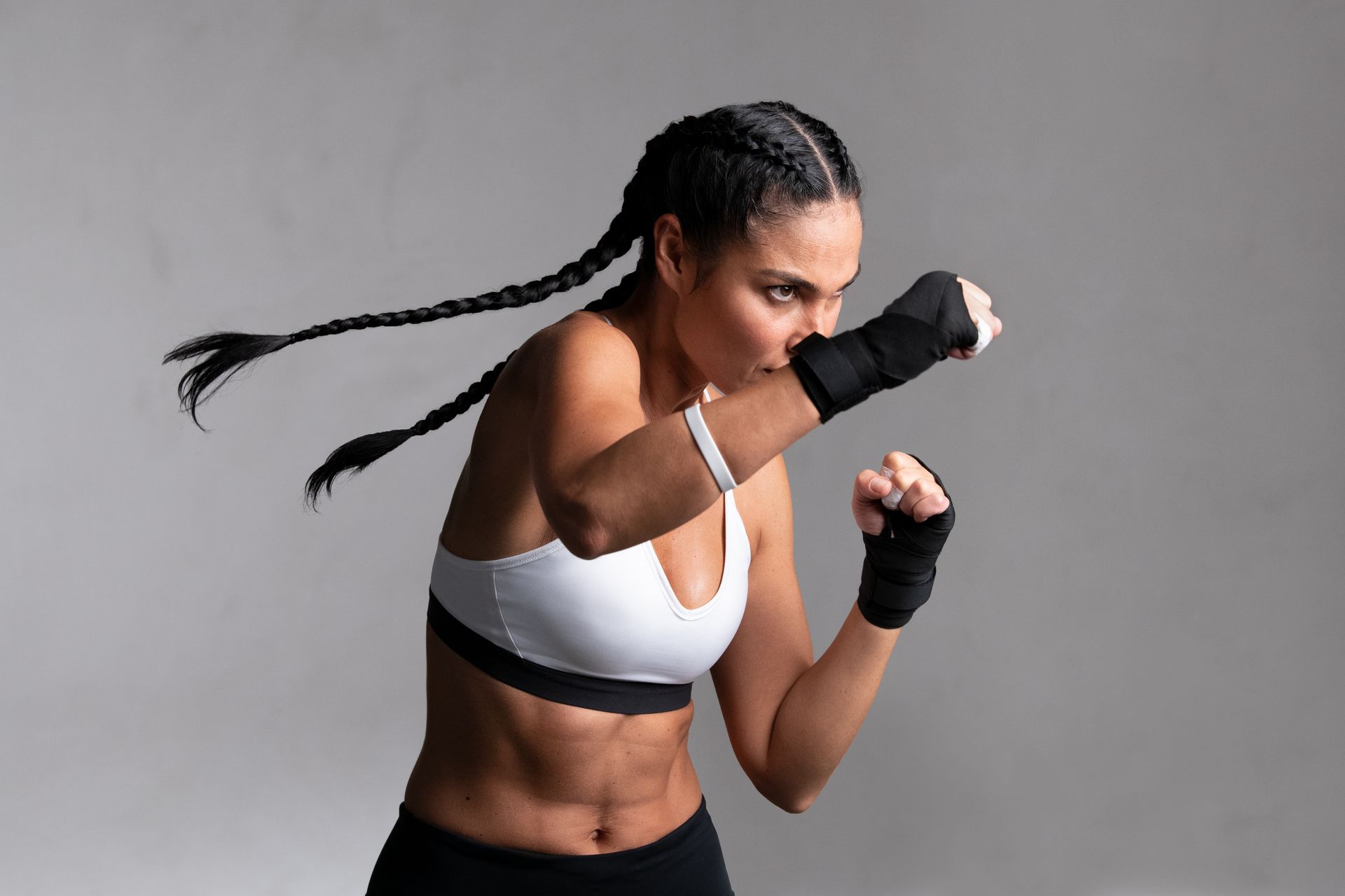 Woman with braided hair in boxing stance, wearing sports bra and hand wraps, punching forward.