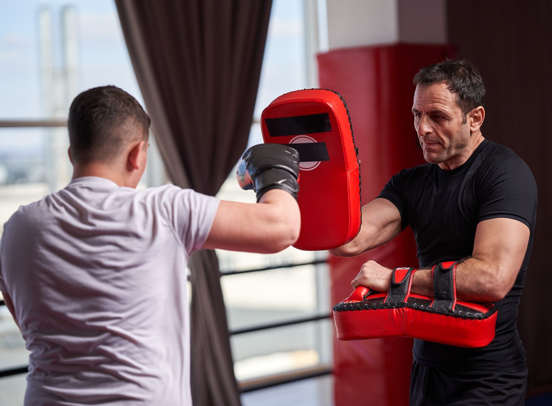 Man training with a pad held by another person in a boxing gym.