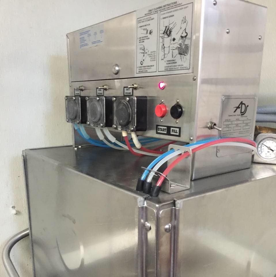 Stainless steel machine with hoses, buttons, and gauges; likely industrial equipment.