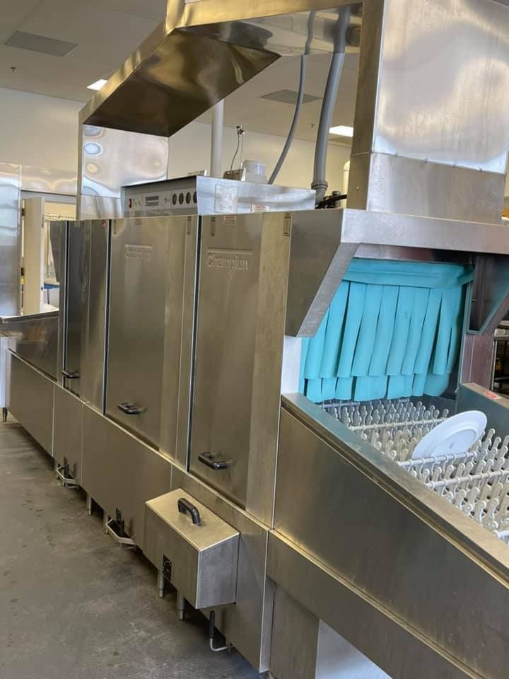 Commercial dishwasher in a kitchen; stainless steel with blue curtains and racks for dishes.