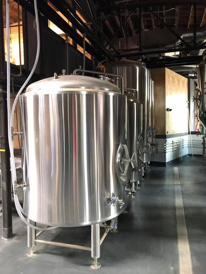 Shiny stainless steel brewery tanks inside a factory setting.