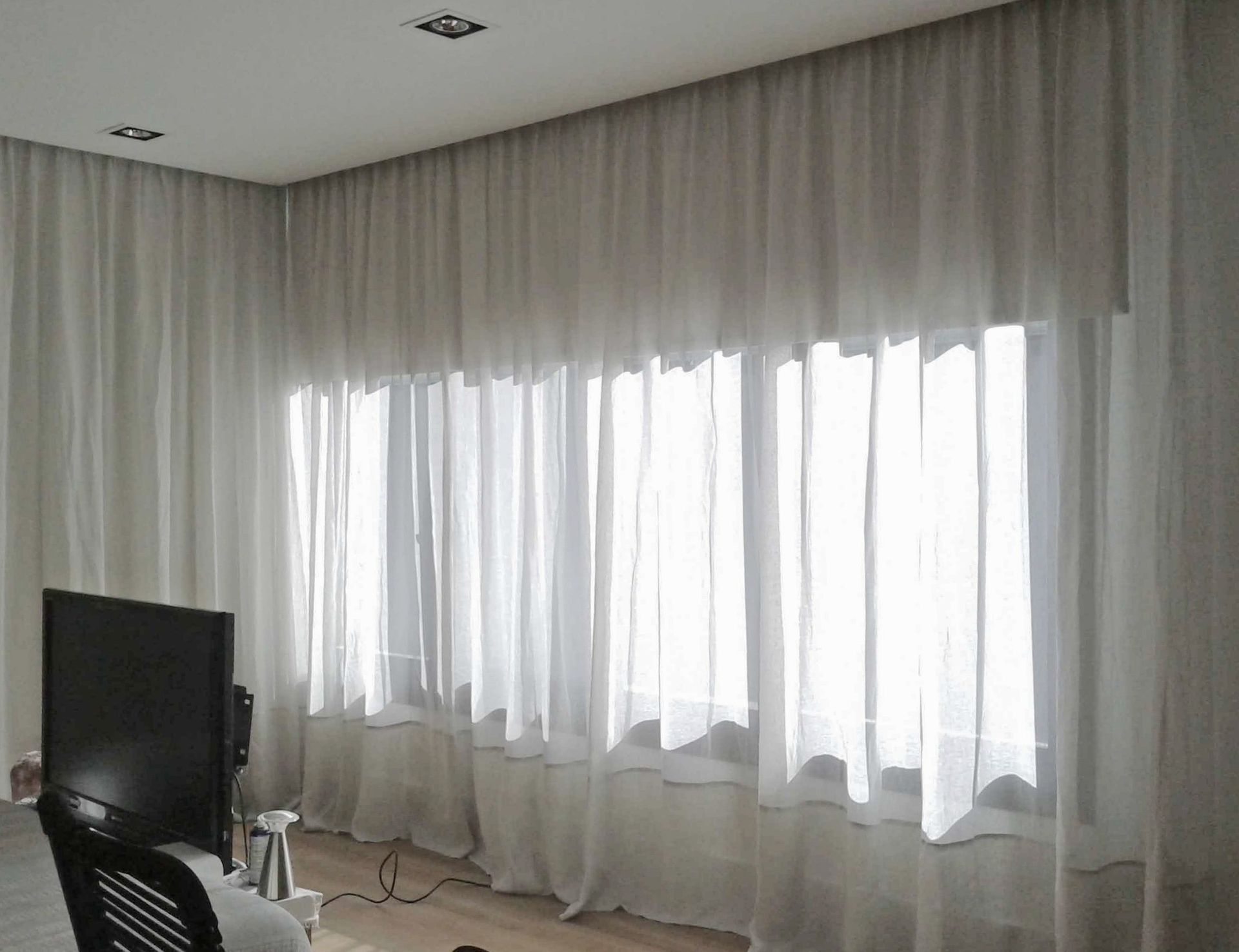 Una sala de estar con cortinas blancas y un televisor de pantalla plana.