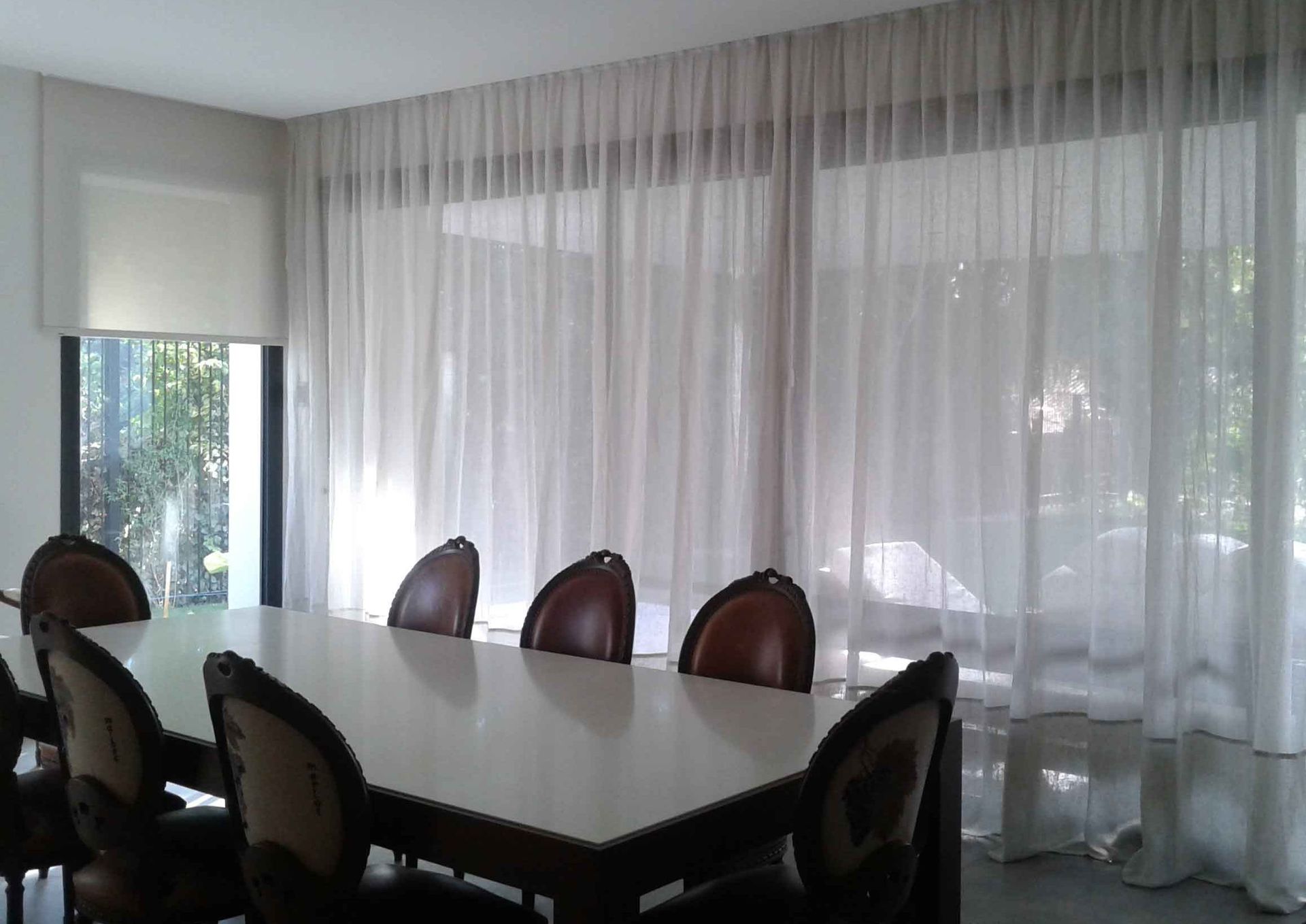 Un comedor con mesa y sillas y cortinas transparentes.