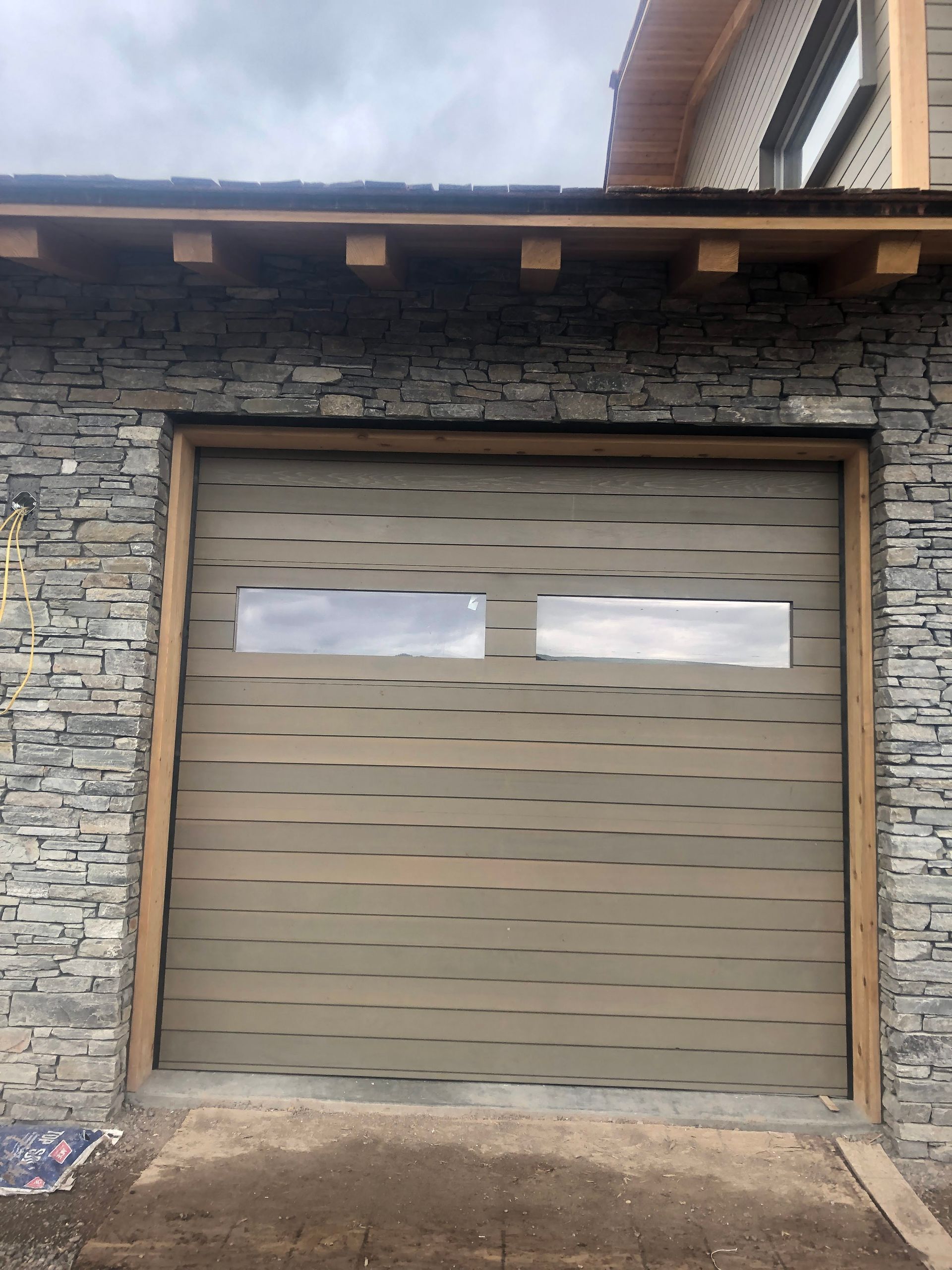 Garage door with horizontal wood grain pattern, two rectangular windows, stone wall exterior.