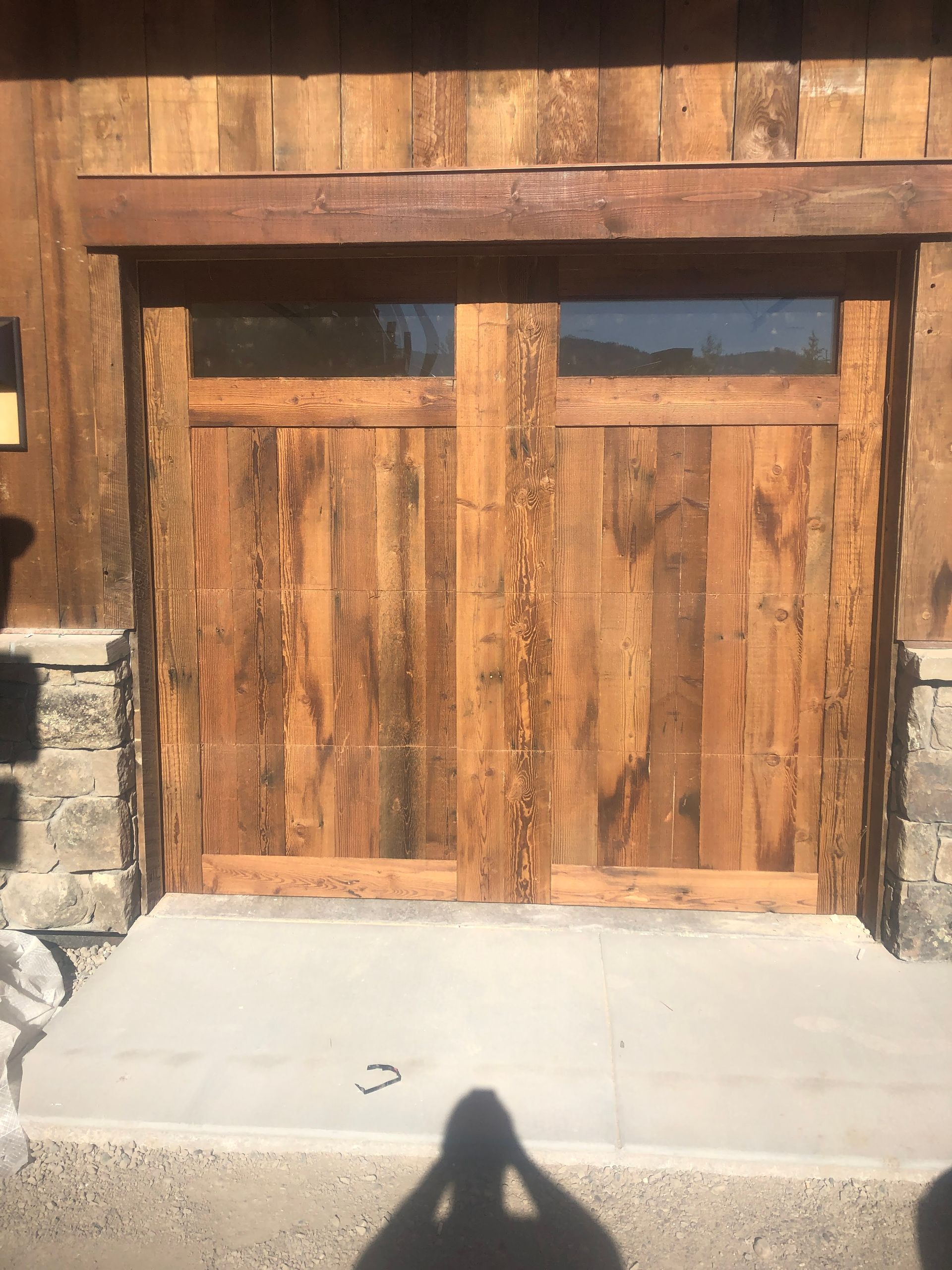 Wooden garage doors with two glass panels above, set in a wood and stone exterior.