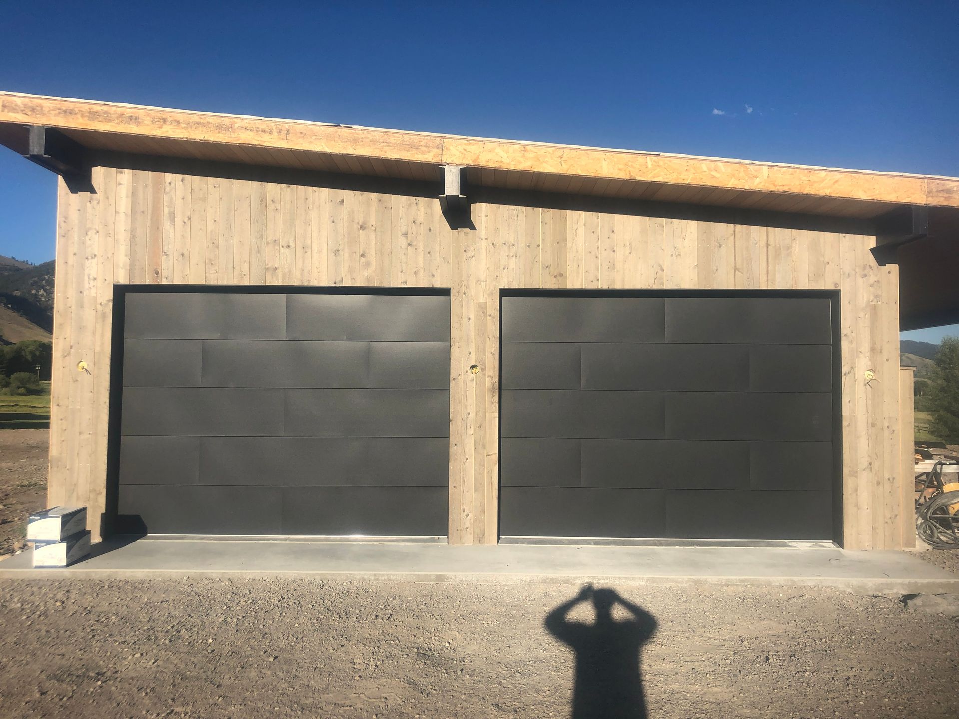 Two dark gray garage doors in a concrete building with exposed wood framing.
