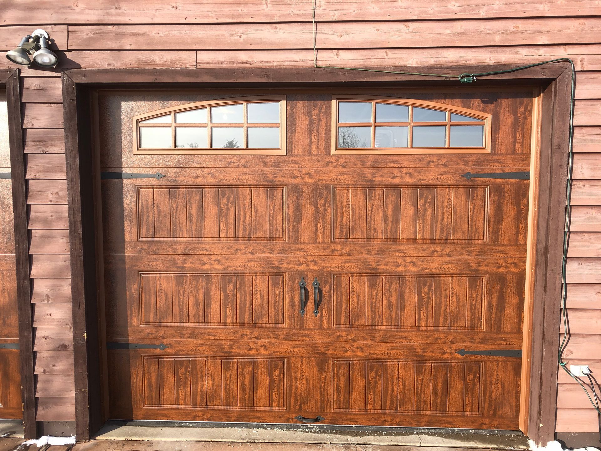 Brown garage door with windows, dark hardware, and wooden textured panels.