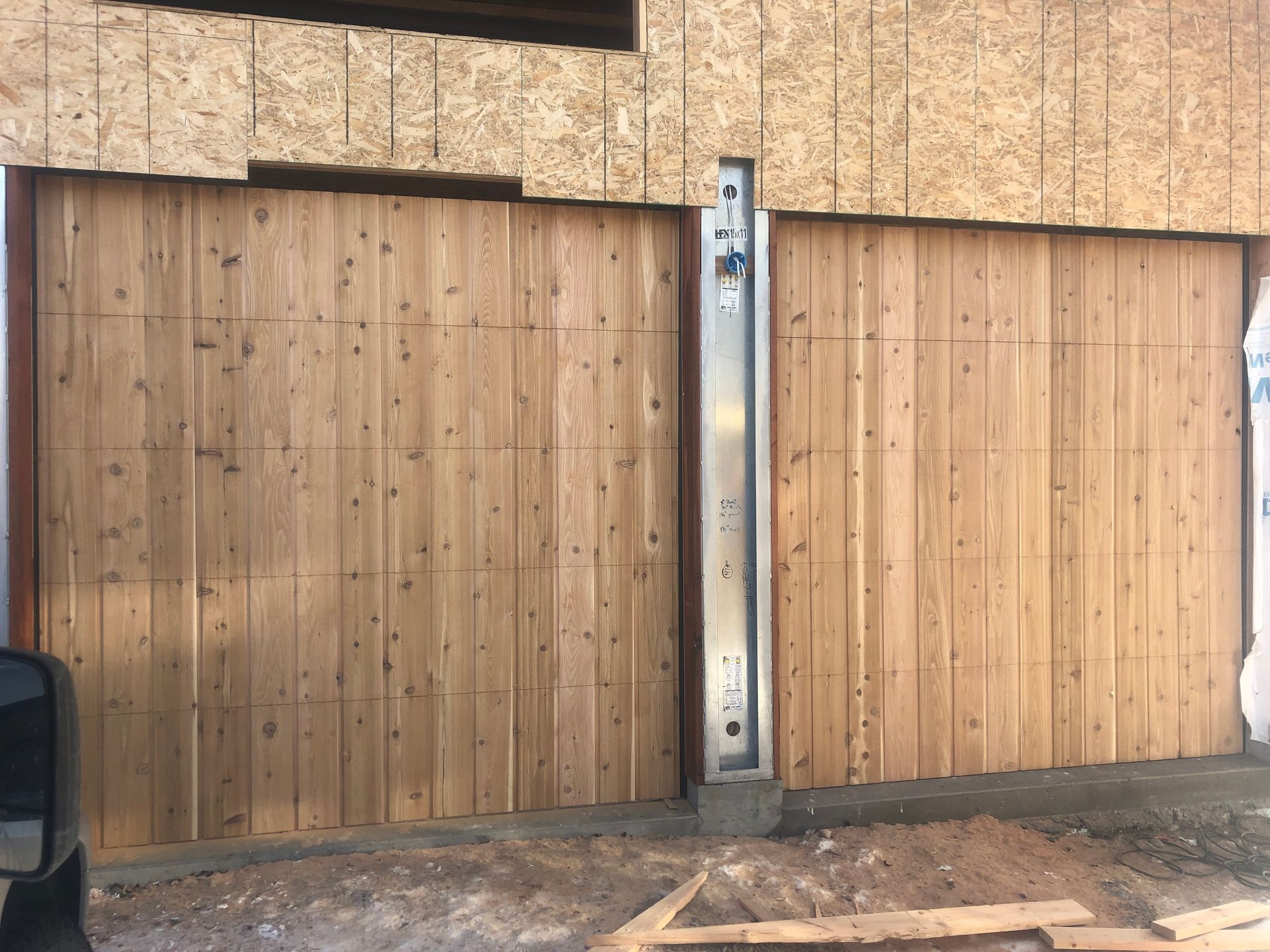 Two wooden garage doors on a building, separated by a metal support.
