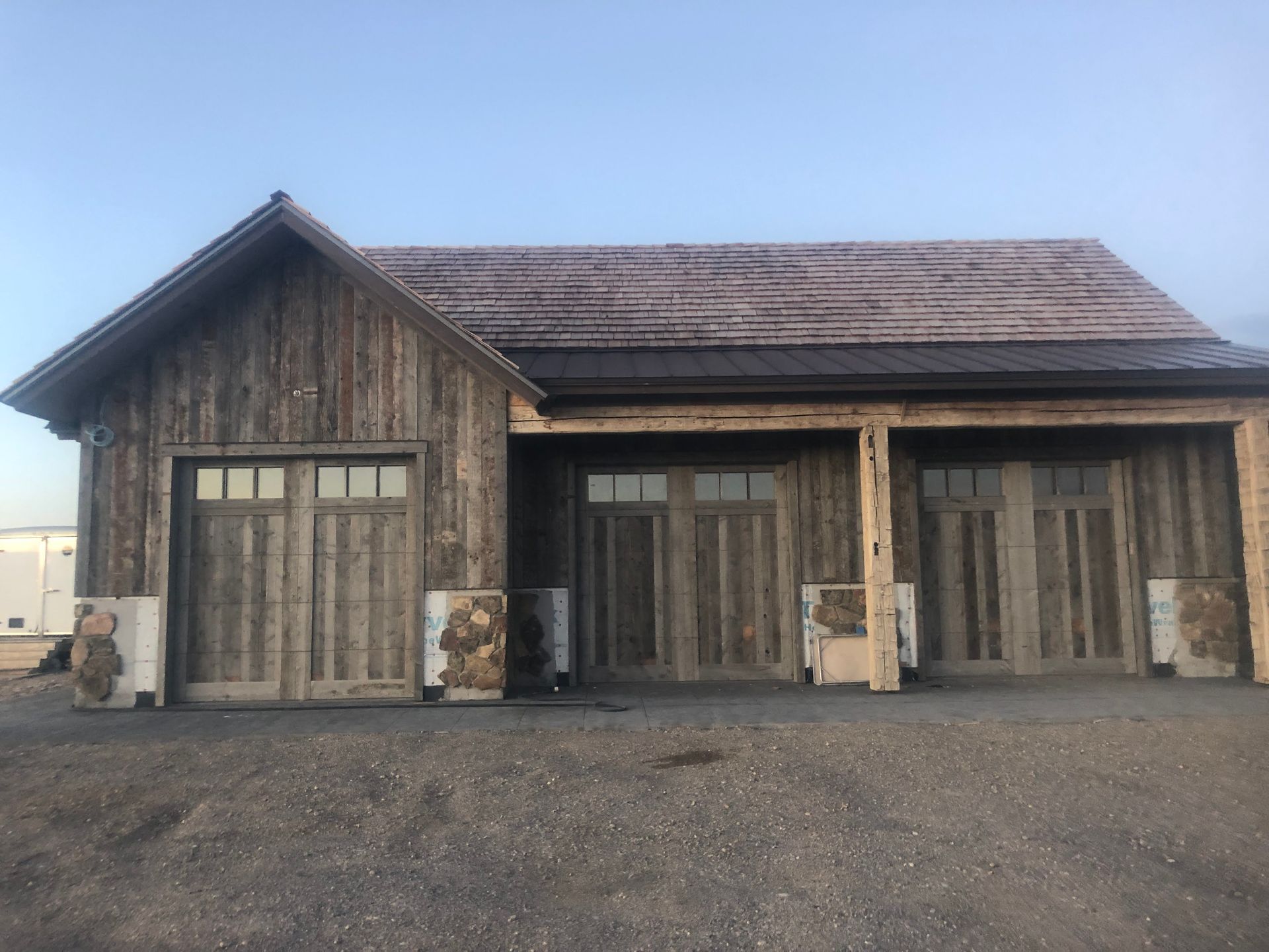 Weathered wooden building with two garage doors and a center entrance under a covered porch.