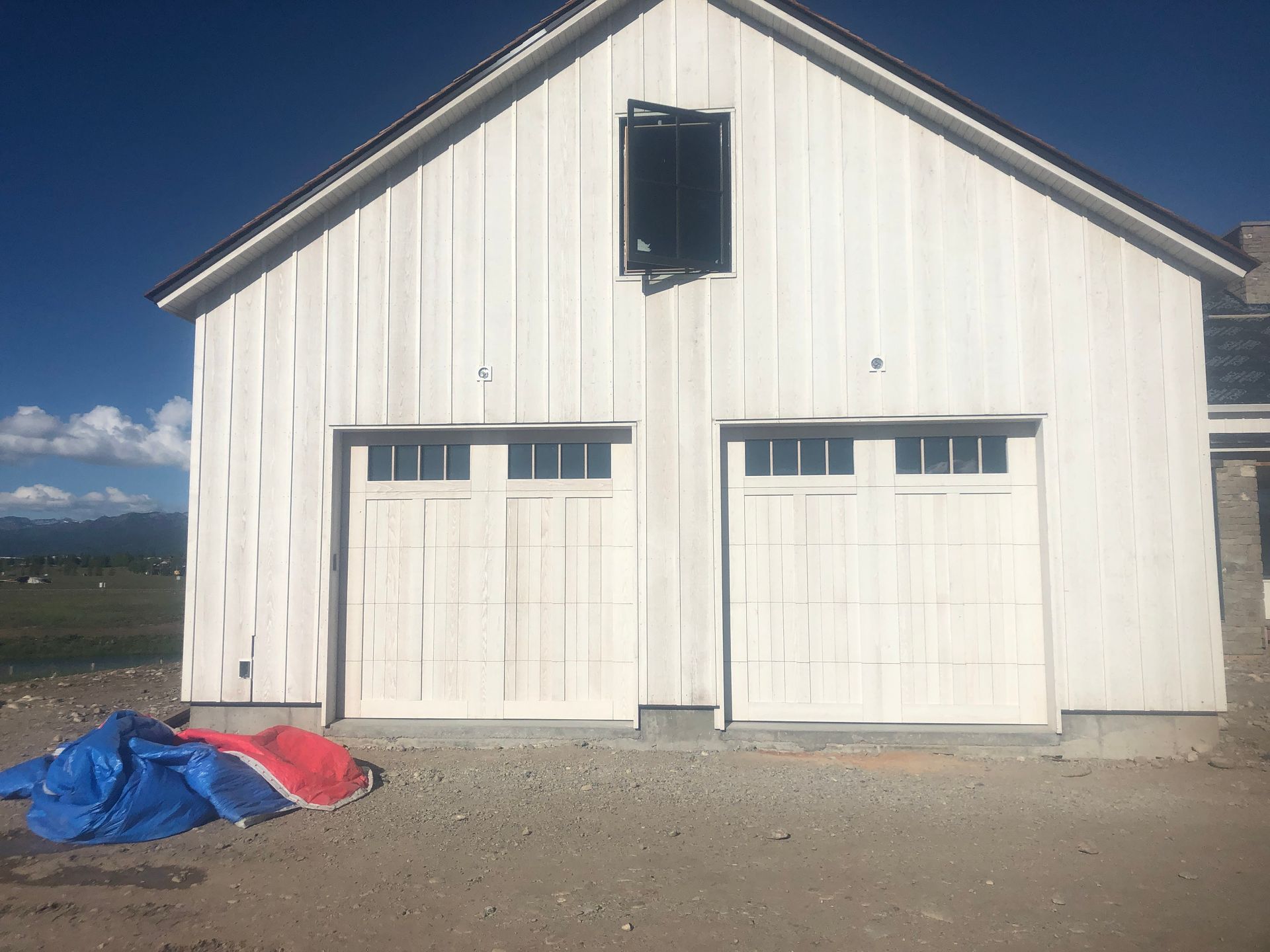 White two-car garage with doors, a window above, and construction materials on the ground.