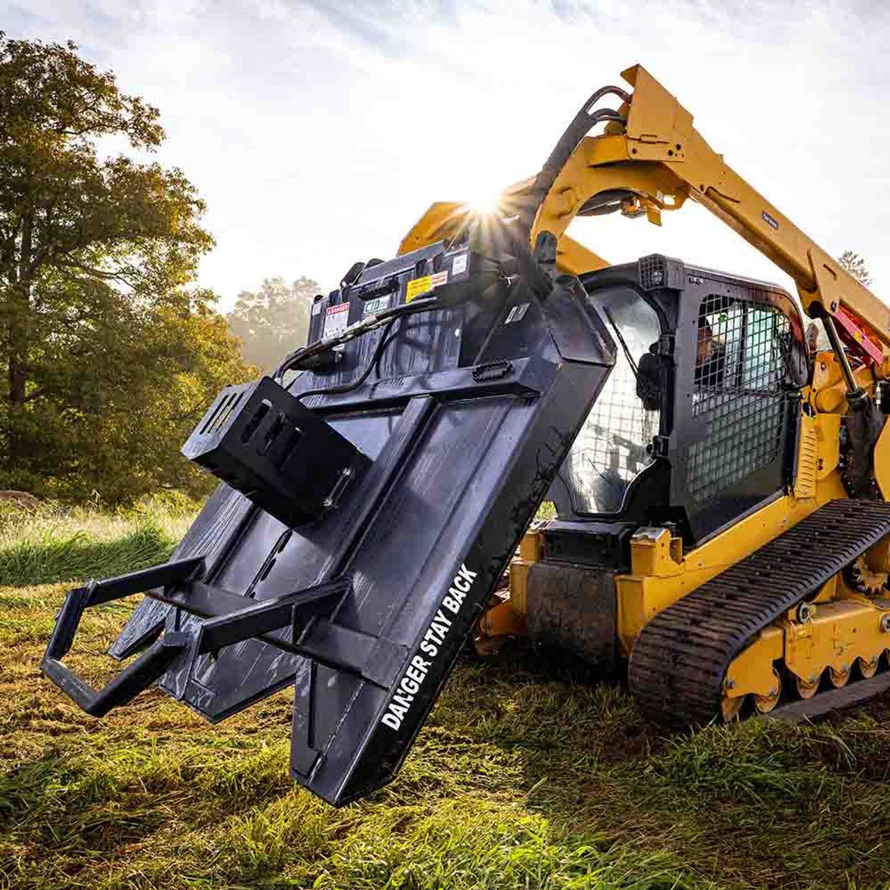 Yellow skid steer with a black forestry mower cutting grass in a field.