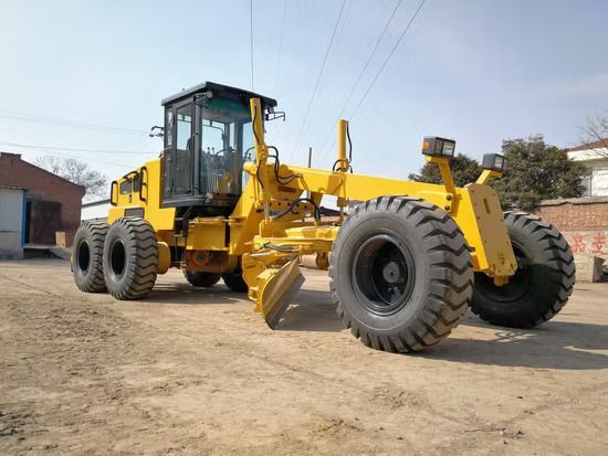 Yellow motor grader on a dirt surface, with a clear sky in the background.