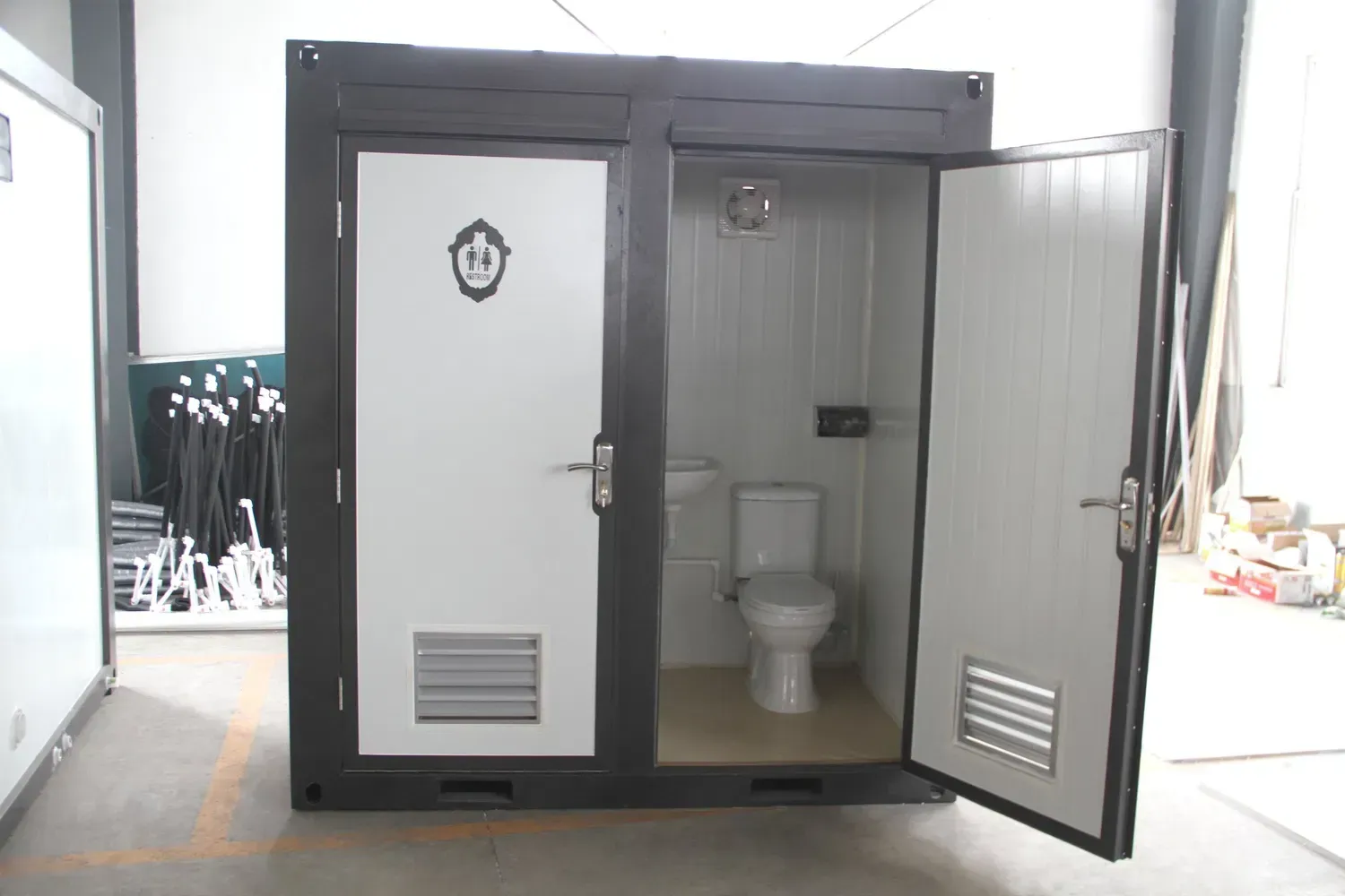 Black and white portable restroom with open door, toilet visible.