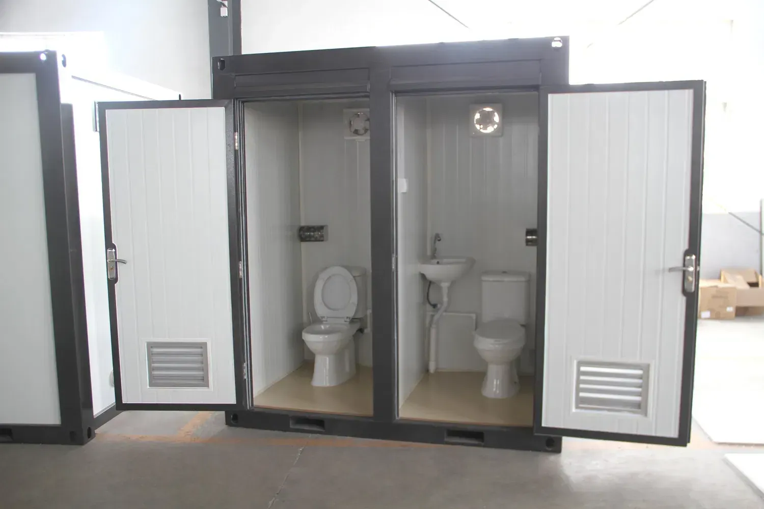 Portable container toilets with white doors and interior, grey exterior, industrial setting.