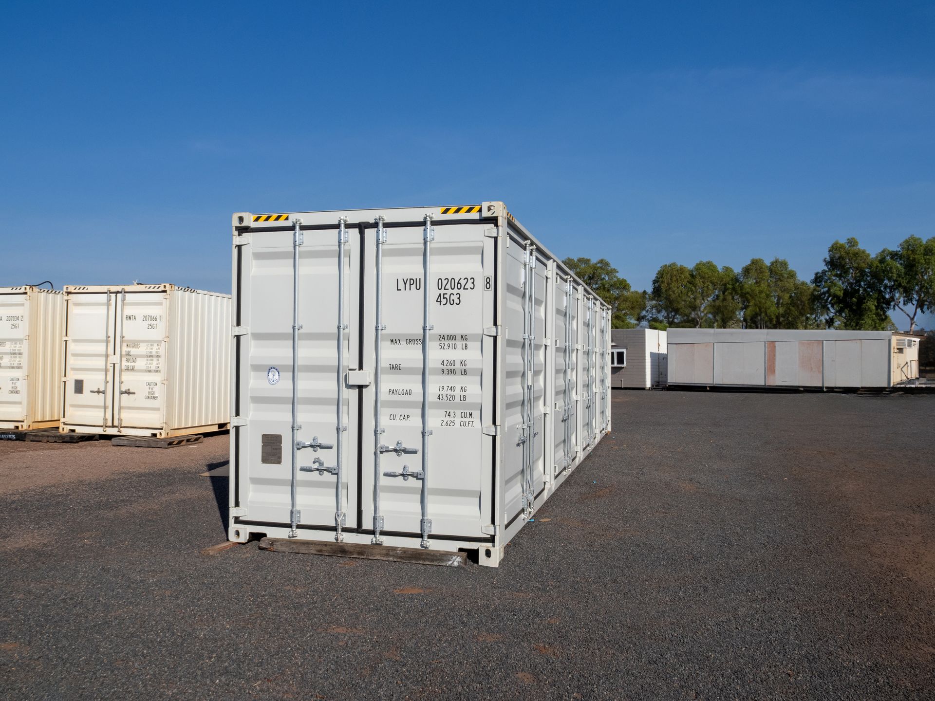 White shipping containers in a gravel lot under a clear blue sky.