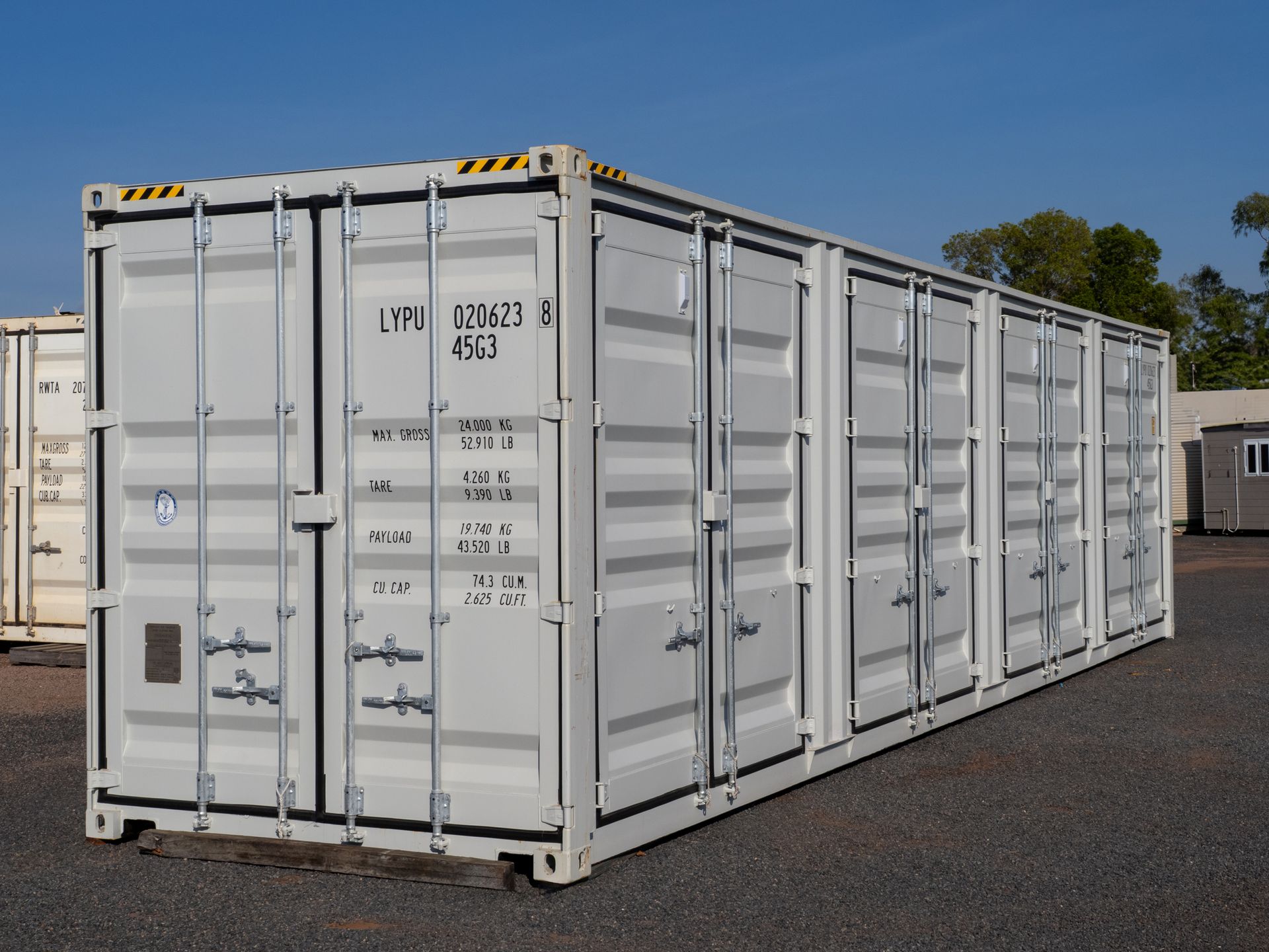 White shipping containers lined up on a gravel surface against a blue sky.