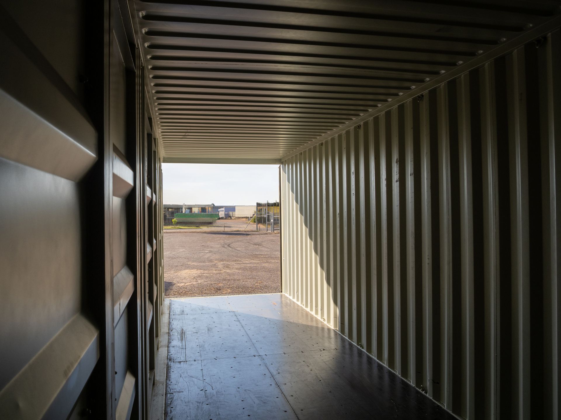 Interior view of a shipping container, with a bright opening to an outdoor area with other objects.