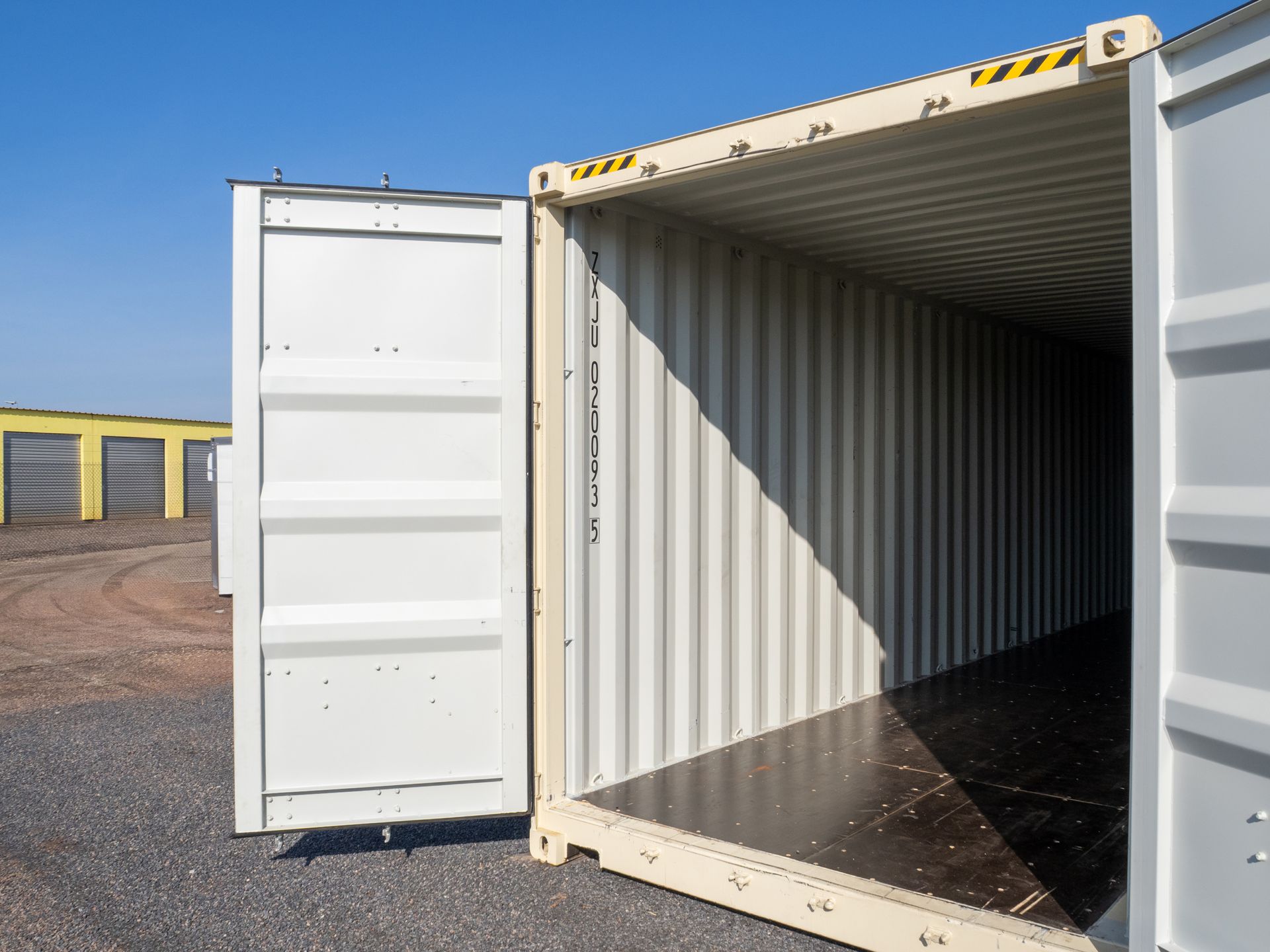 Open, empty off-white cargo container; corrugated metal walls; dark floor. Outdoors.