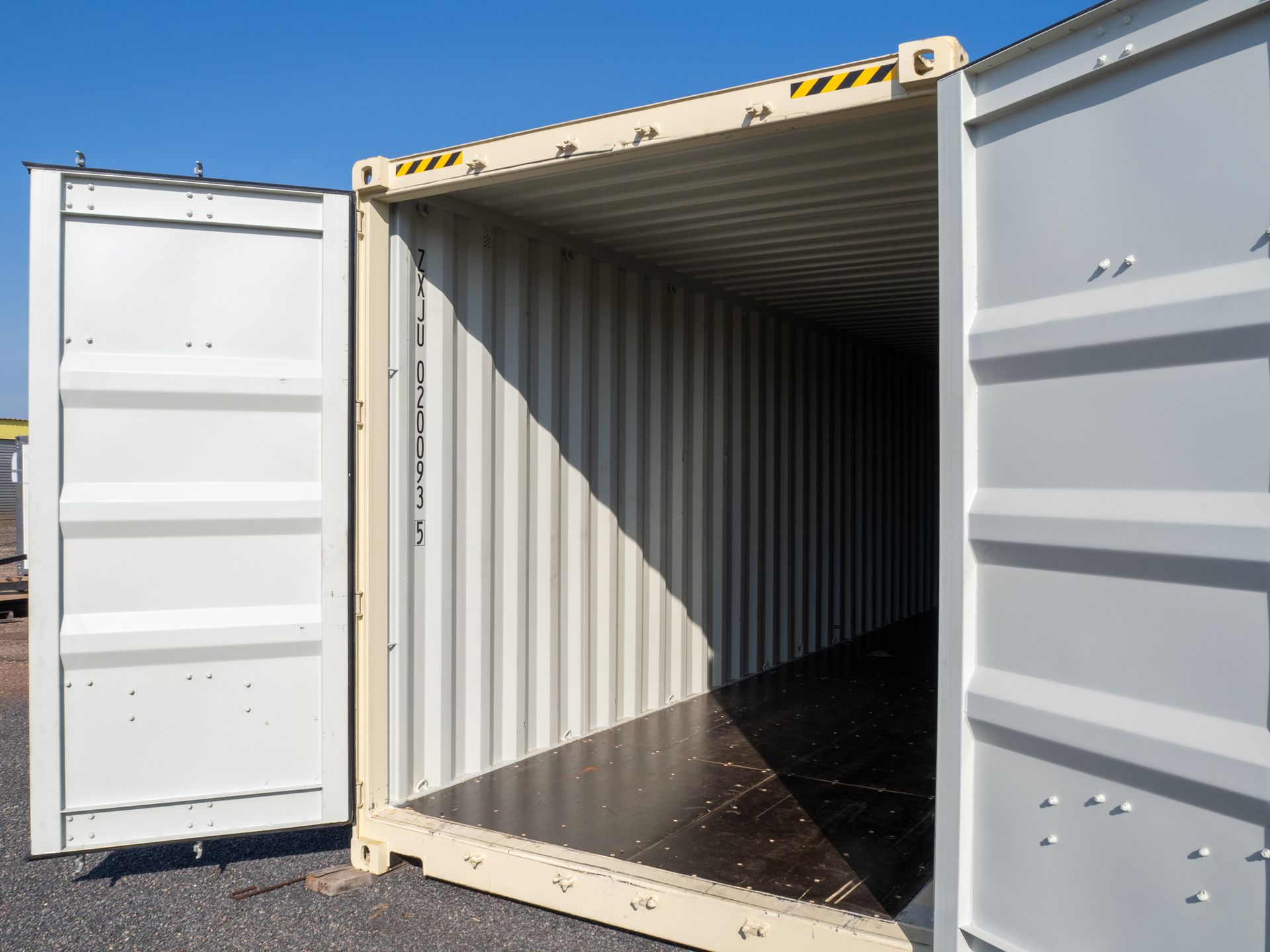 Open beige shipping container doors, dark interior, sitting on pavement.