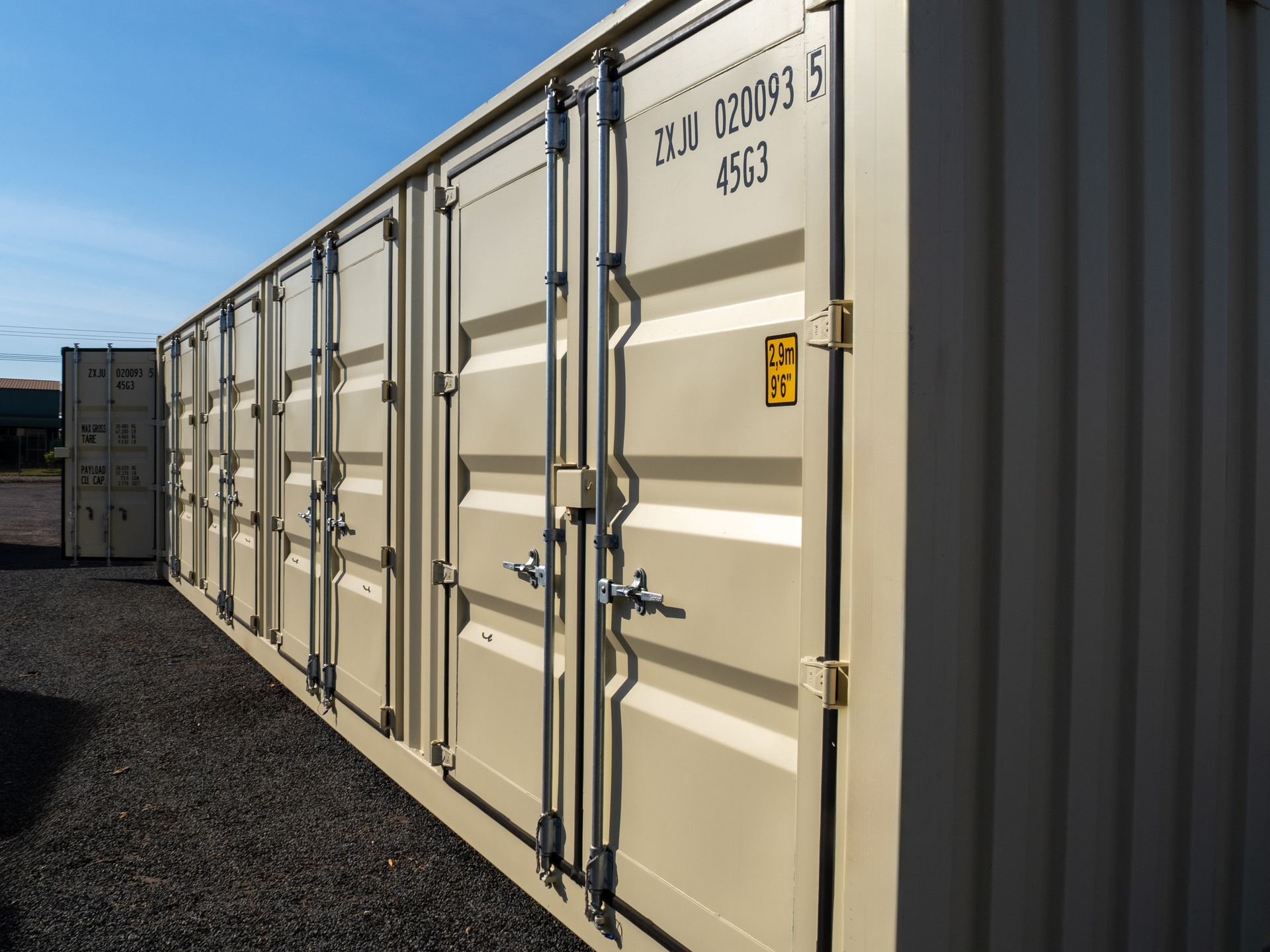 Beige shipping containers lined up outdoors, blue sky background.