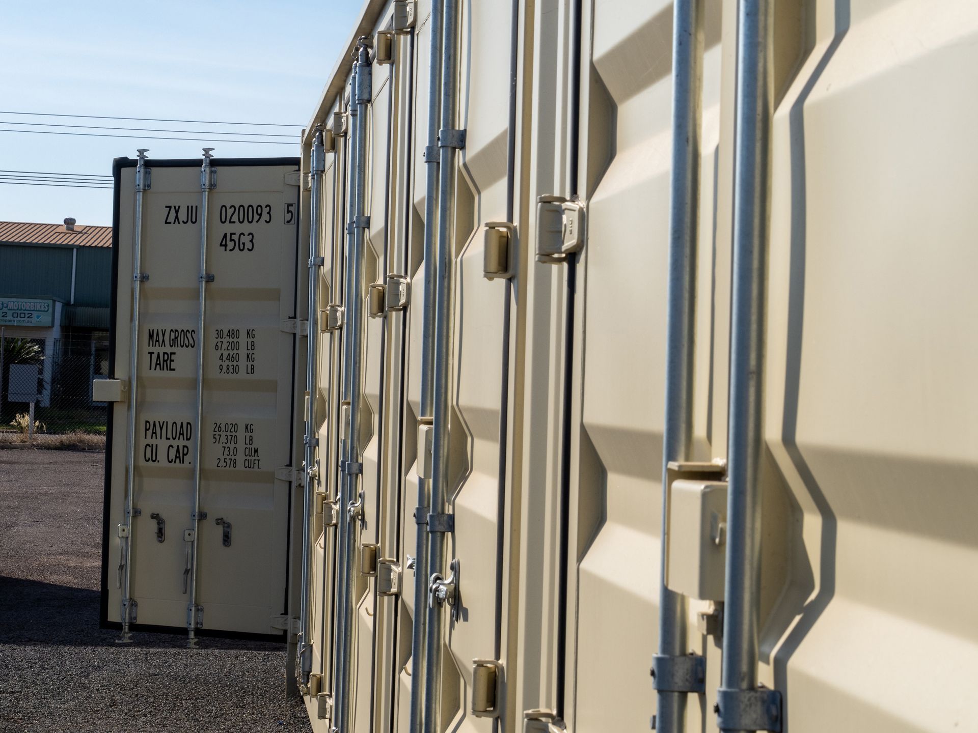 Tan storage containers in a row, outdoors. One is open.