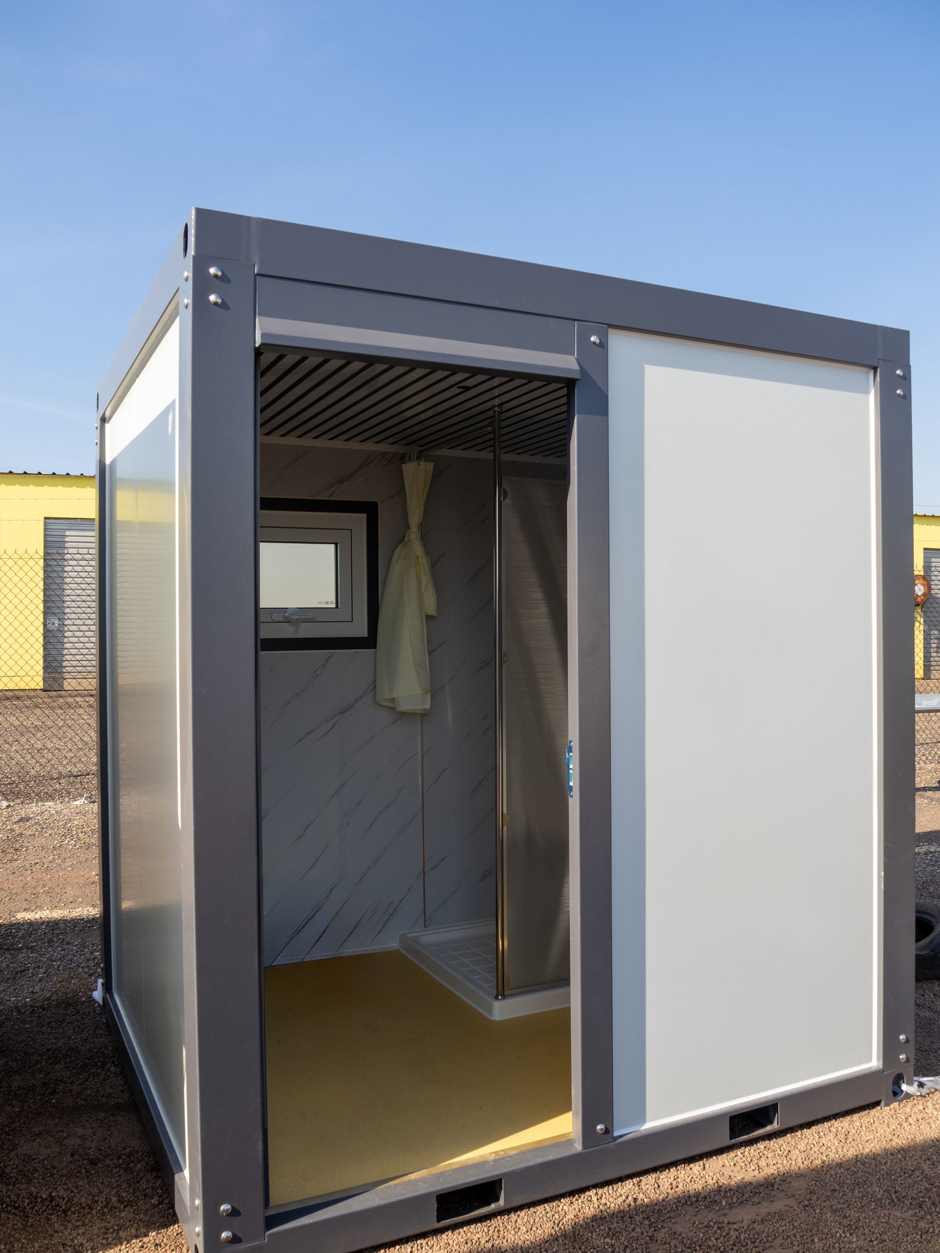Gray portable shower unit with sliding door, yellow floor, and window.