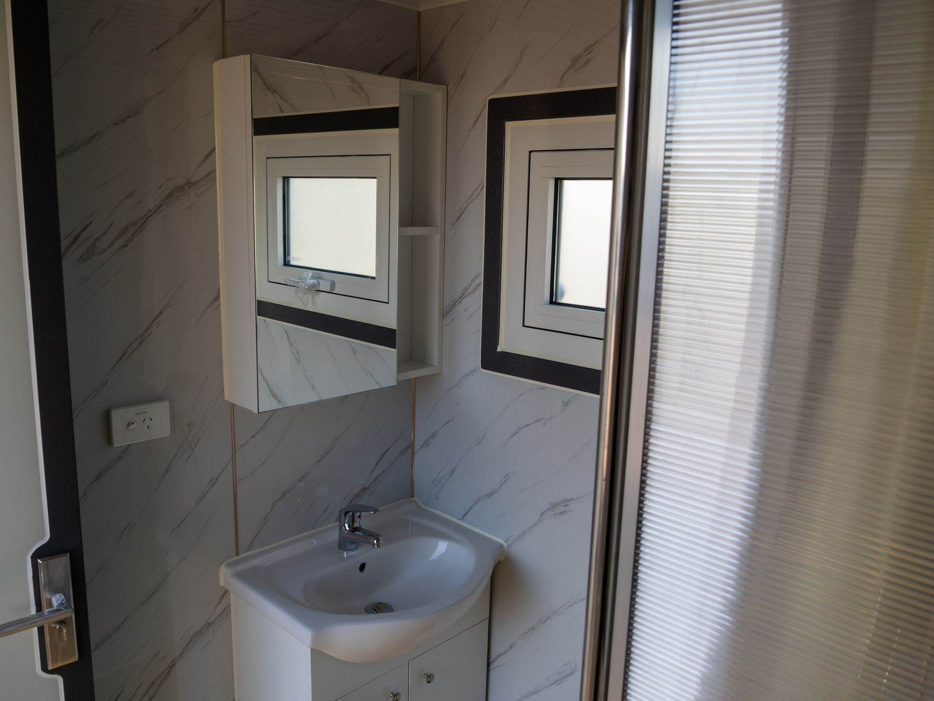 Bathroom with vanity, mirror, window, and shower. White and gray tile with a clean modern aesthetic.