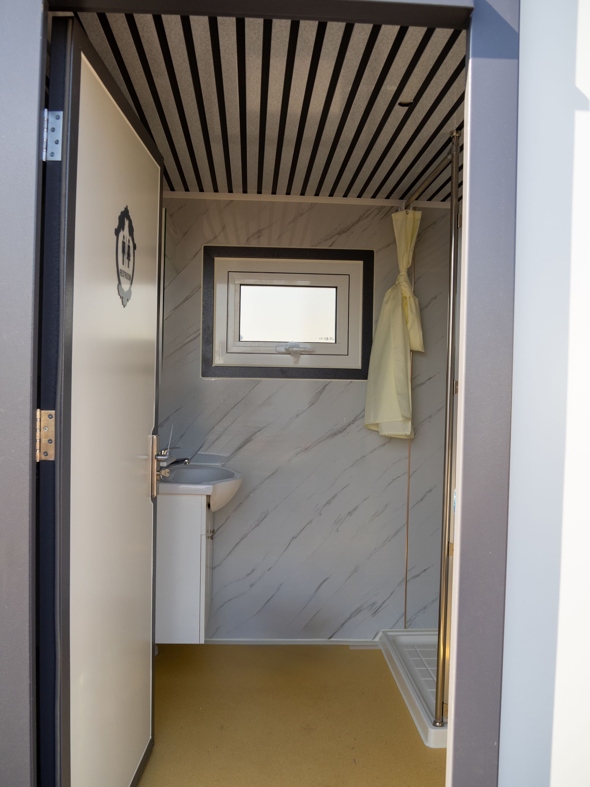 Open doorway into a small bathroom with a sink, window, and shower curtain; yellow floor, marble-look walls.