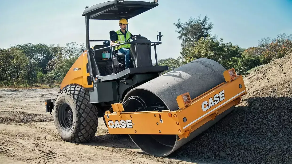 Yellow CASE roller compacting gravel with operator.