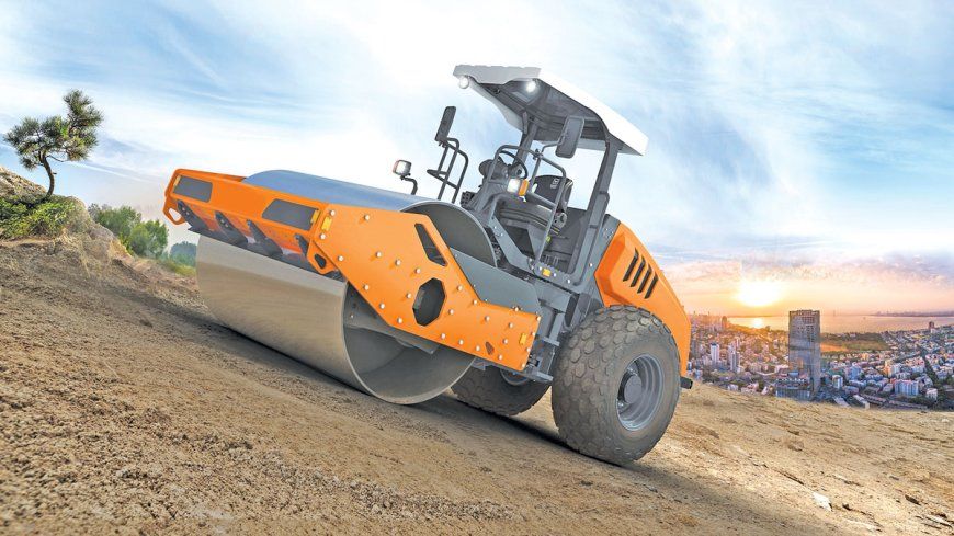 Orange and gray road roller compacting dirt on a hillside under a blue sky.