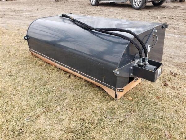 Black skid steer broom attachment on grass, with hydraulic lines.