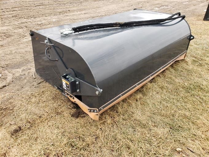 Black hydraulic-powered sweeper attachment on a field.