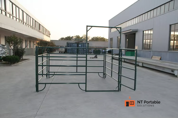 Green metal livestock gate system outdoors near industrial buildings.