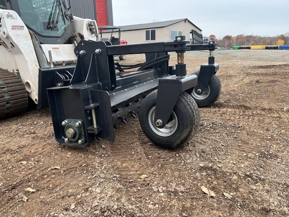 A black landscape rake attachment on a skid steer, preparing soil.