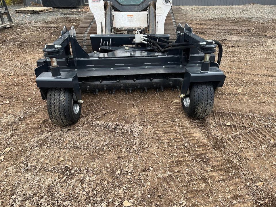 Skid steer with a black landscape rake preparing soil outdoors.