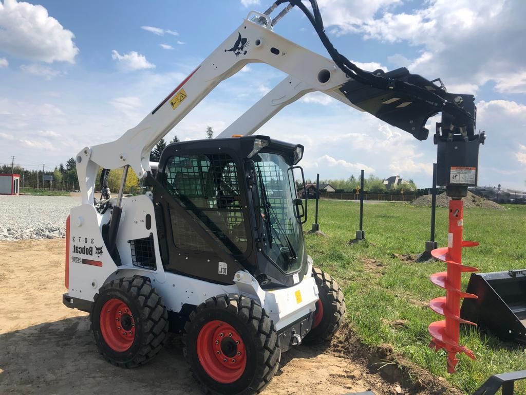 White Bobcat skid-steer loader with auger attachment drilling a hole in the ground.