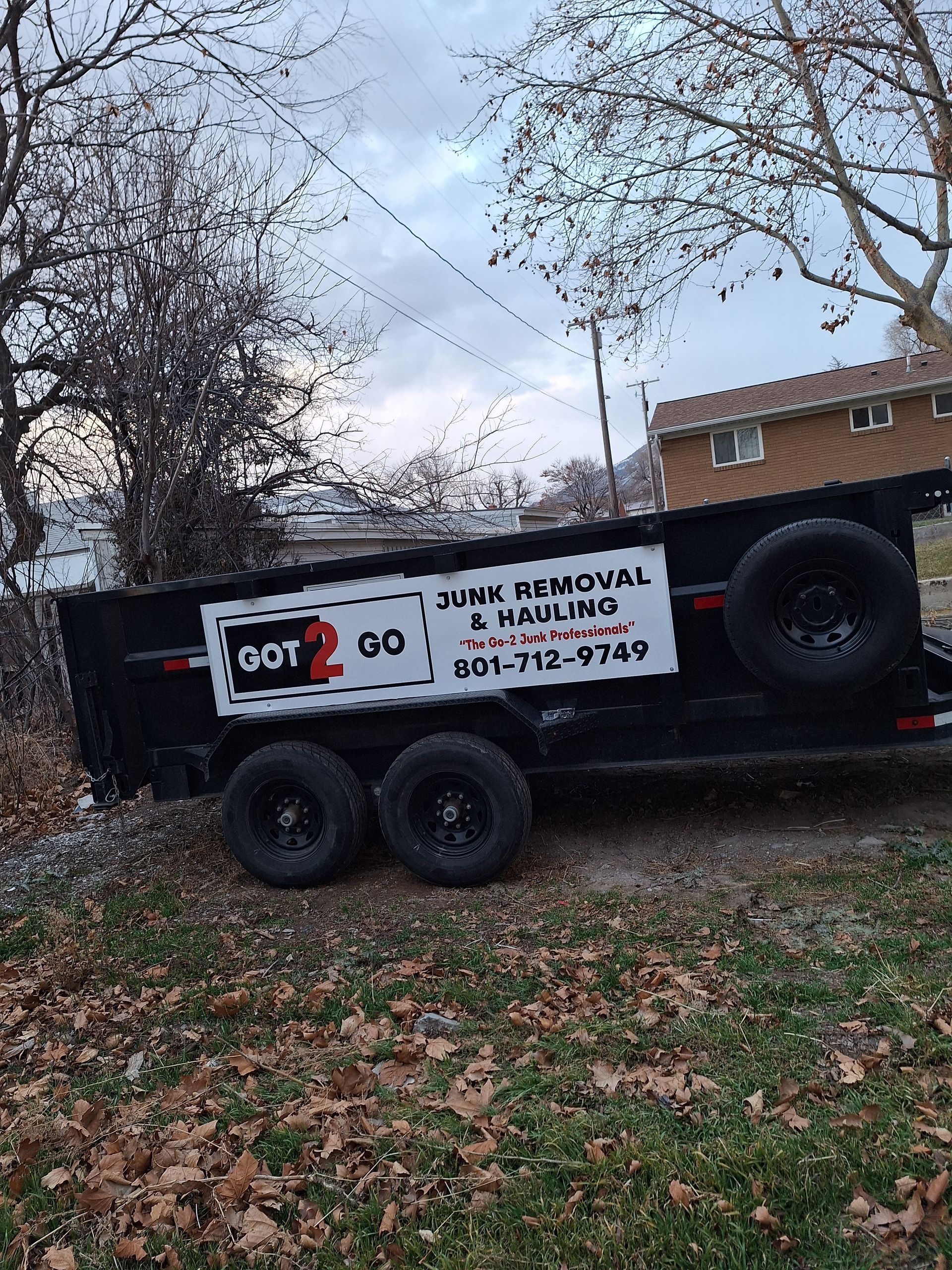A gray utility trailer with a high-sided bed, parked on a paved road.