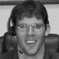 Man wearing glasses and a headset smiles, indoors.