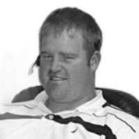 Man in a wheelchair, smiling, wearing a polo shirt, and looking at the camera.