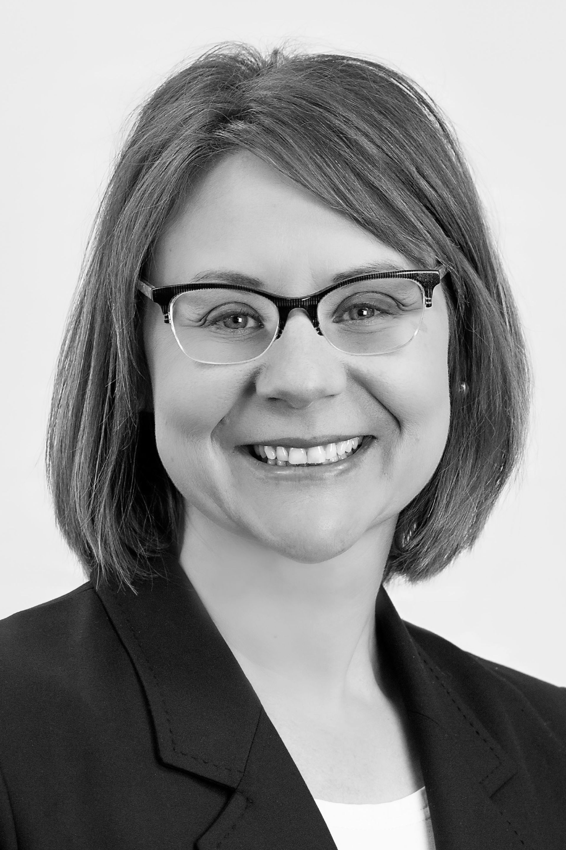 Woman with glasses smiling, wearing a dark blazer.
