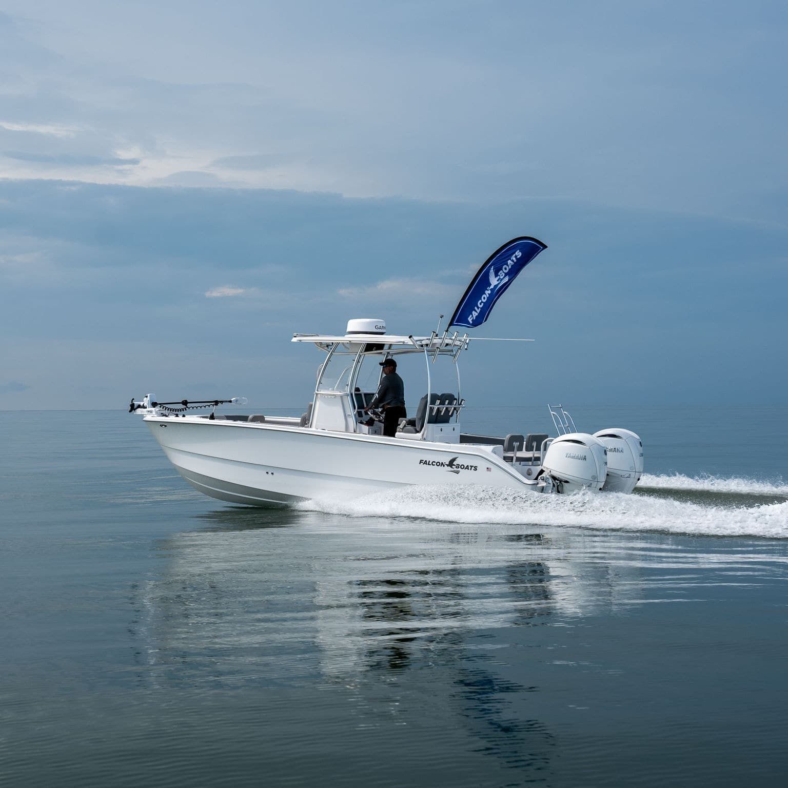 White motorboat speeding on blue water, with people visible. Blue sky with clouds and trees in the background.
