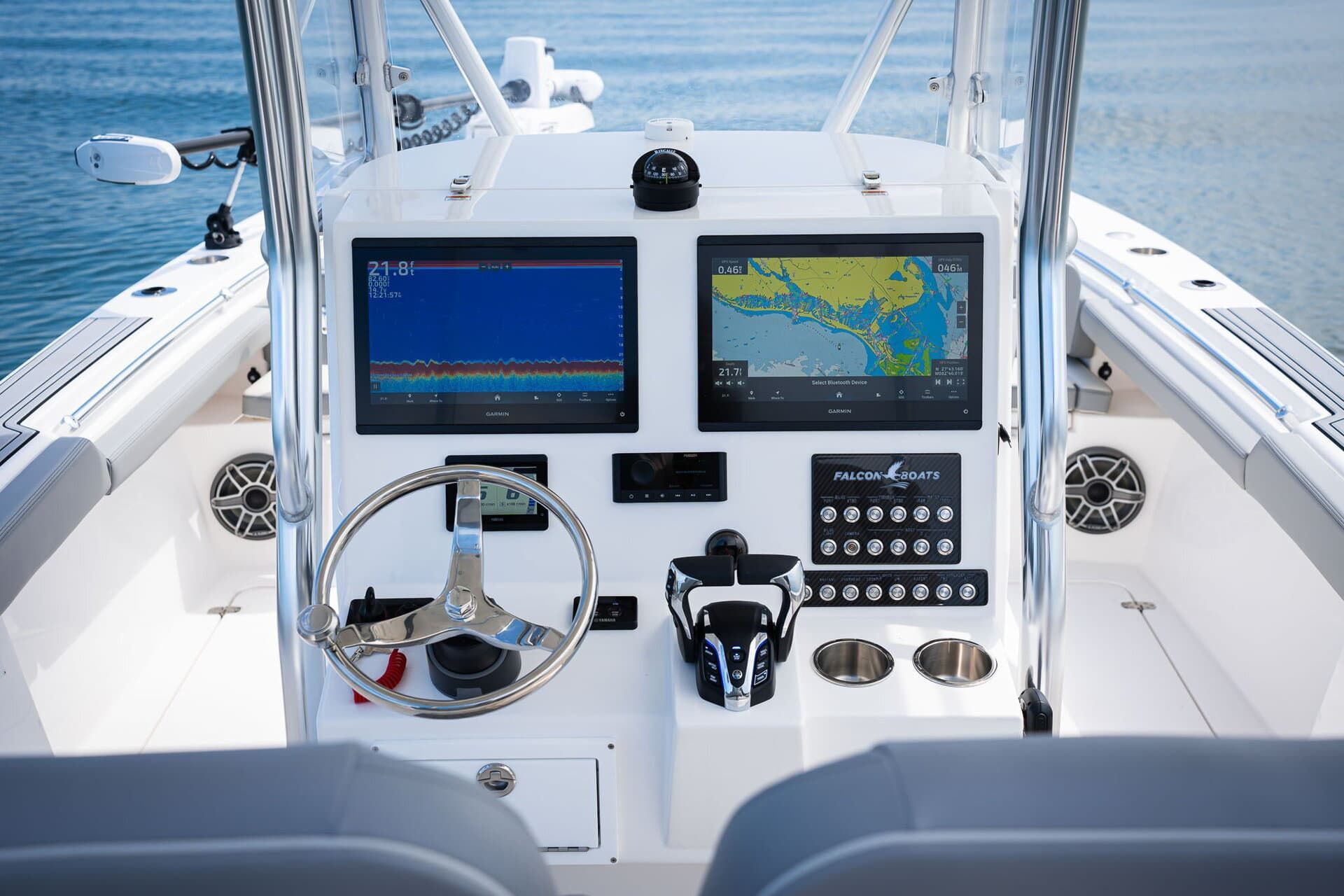 A boat's helm, with a blue console holding gauges and switches, a steering wheel, and views of the water.
