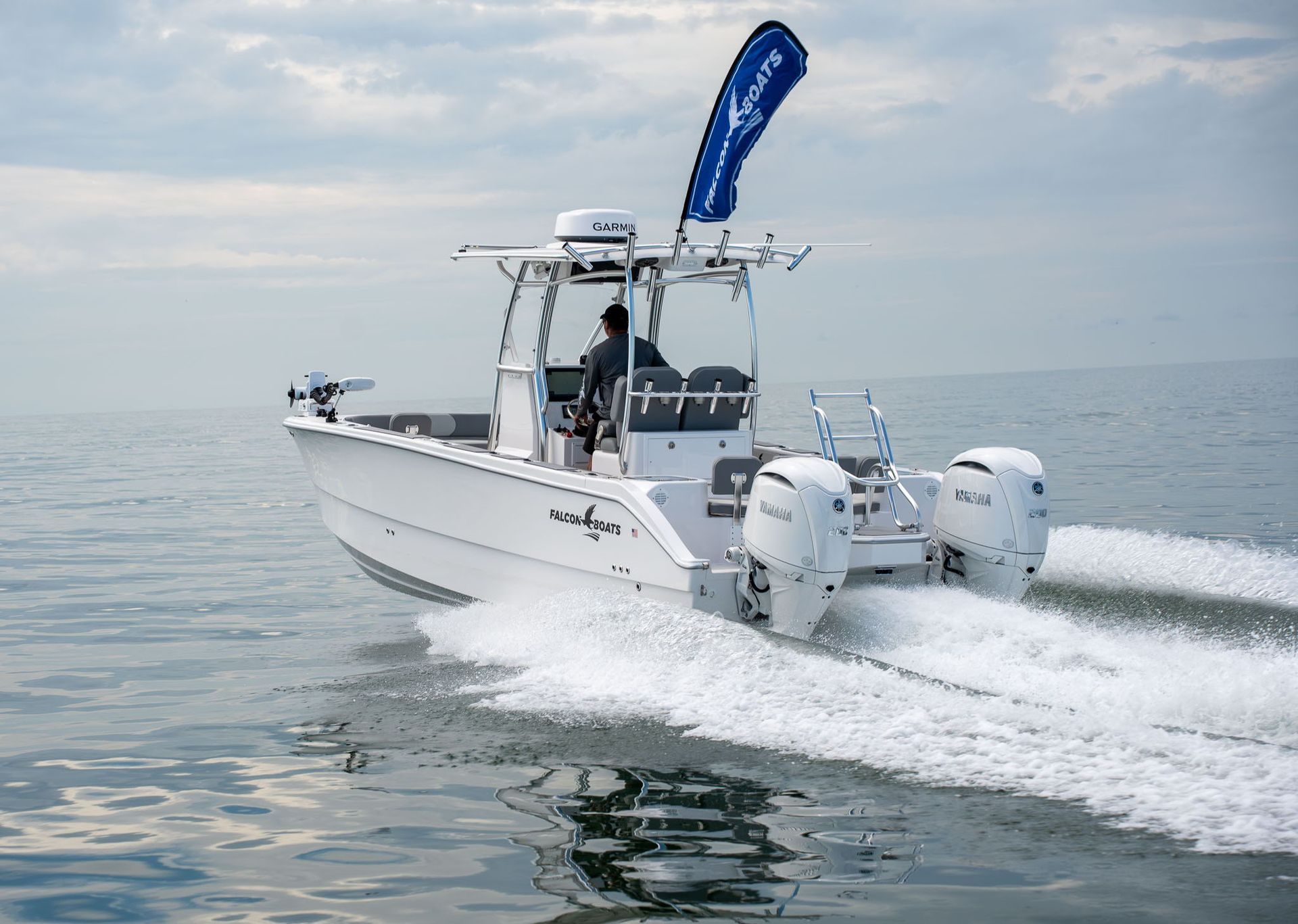 A blue and white catamaran boat floats on turquoise water near a waterfront with shops and restaurants under a sunny sky.