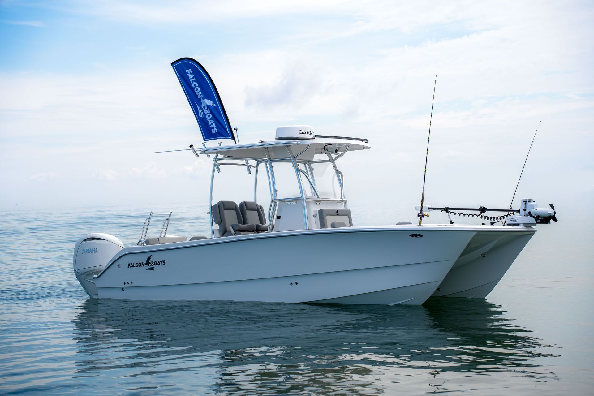 A white and blue catamaran boat floats on turquoise water in front of a vibrant waterfront town under a sunny sky.