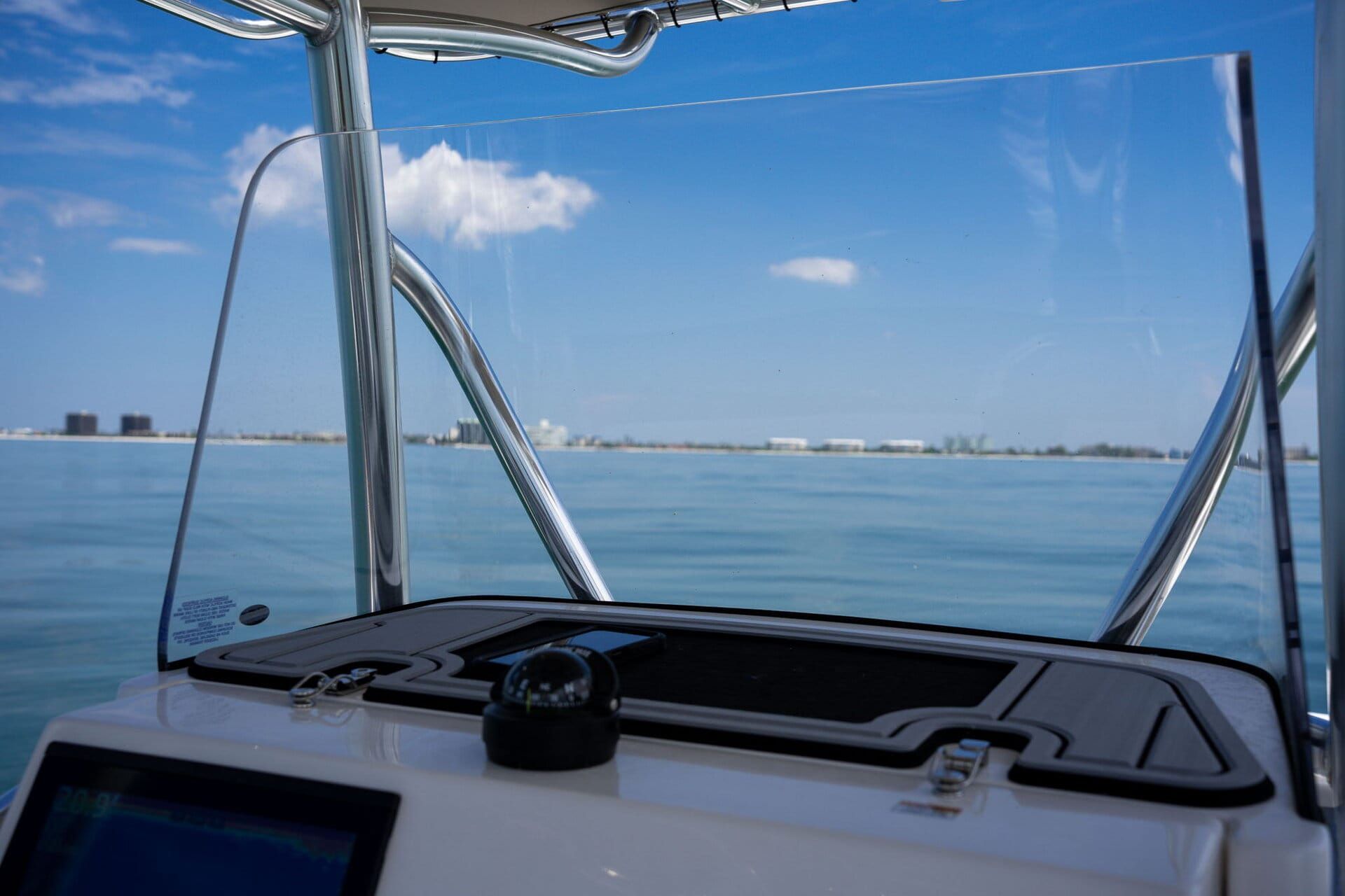View from inside a white boat showing grey and blue seating, docked in a marina. A white and silver walkway is in the background.