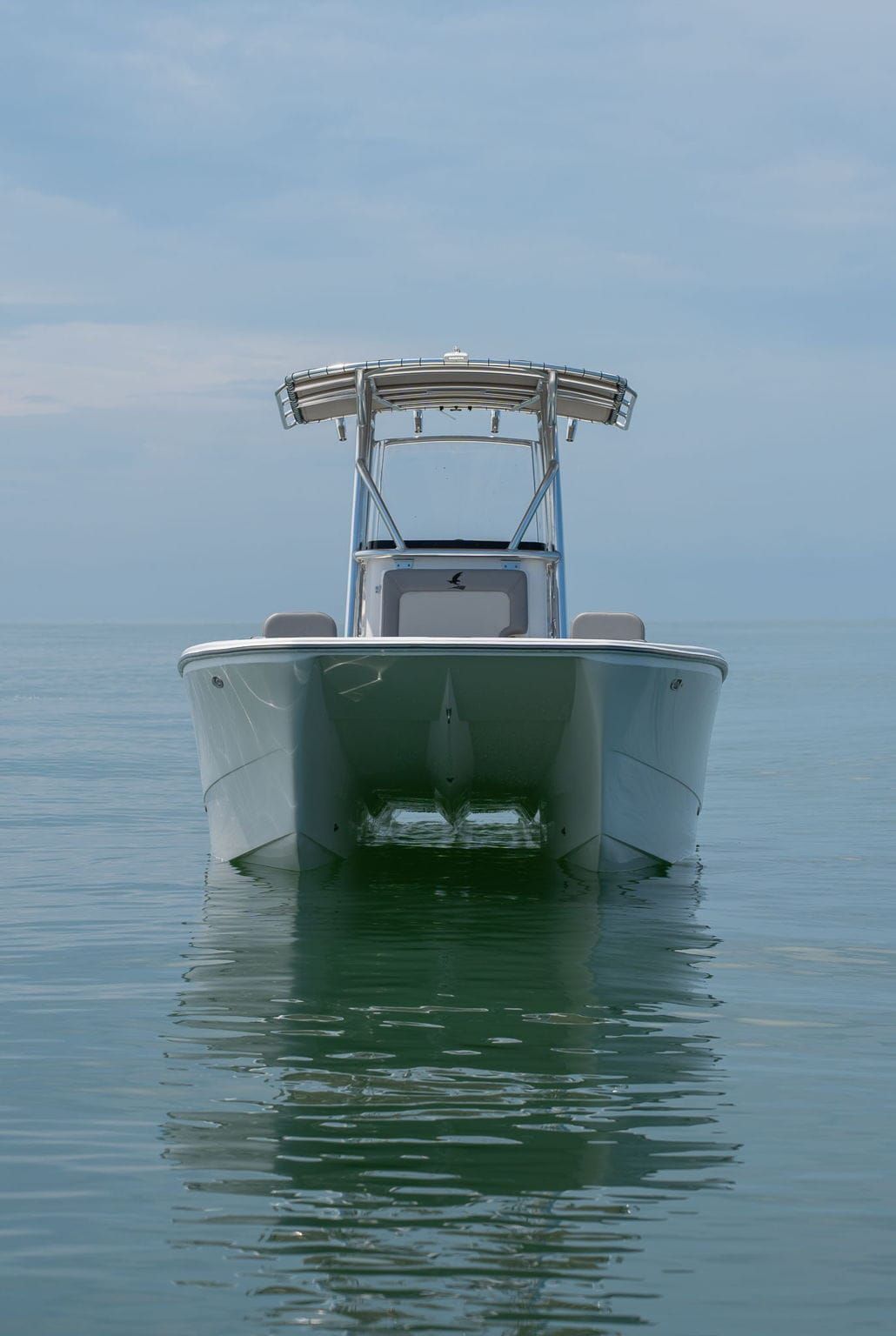 A center console boat with a black and blue design floats in shallow, turquoise water under a cloudy sky.