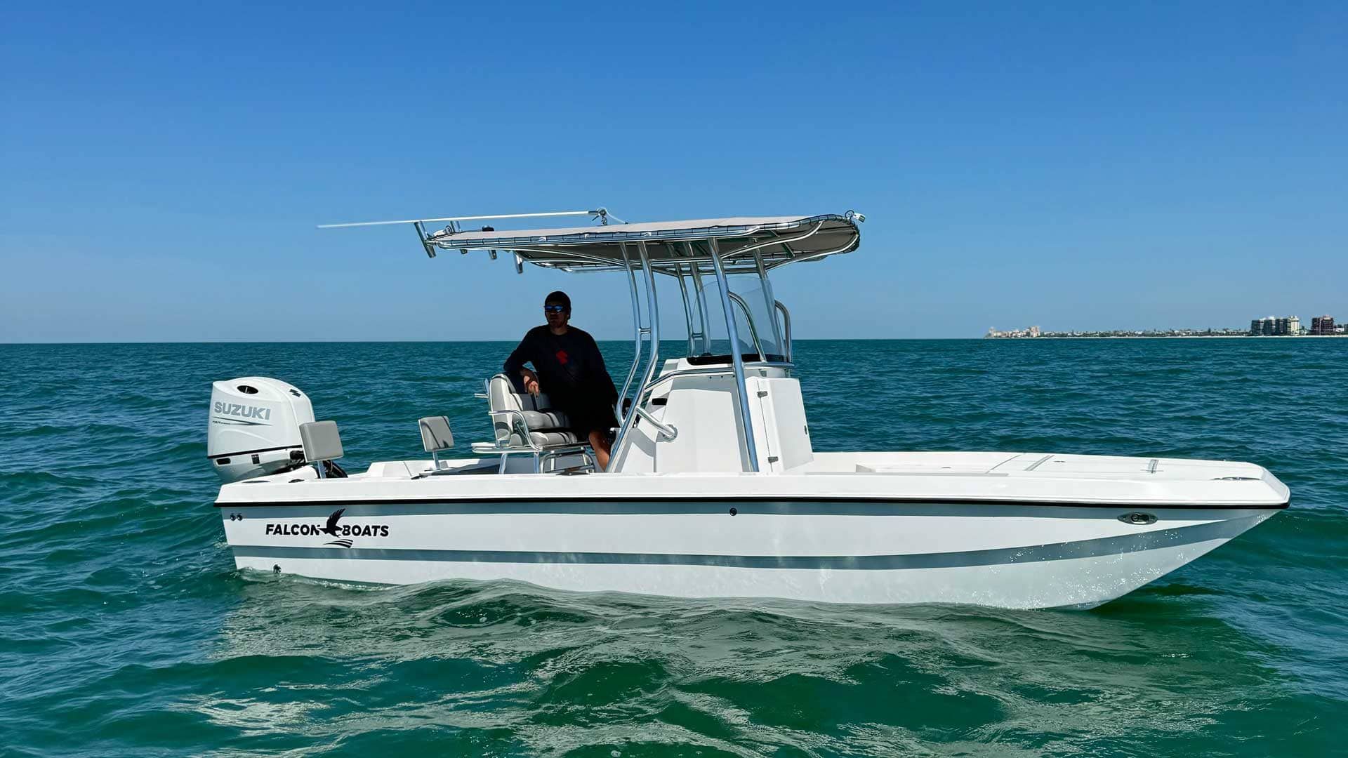 A white motorboat on turquoise water, with a person at the helm under a metal frame.